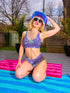 Bralette-style bikini top featuring a high neckline and vibrant jellyfish print in iridescent purples, blues, and greens on a lilac background. Made of recycled polyester and LYCRA XTRALIFE, this double-layered swim top includes removable padding, UPF 50+ protection, and is available in sizes XS to 3XL. Great for raves, beach days, and summer festivals.